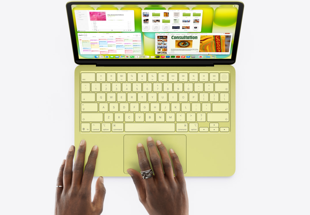 Prikaz MacBooka Neo u citrusnoj boji, na čijem trackpadu osoba drži ruku, a na zaslonu je otvoreno nekoliko prozora s aplikacijama Glazba, Kalendar i Microsoft Power Point