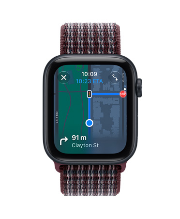 Apple Watch SE 3 éjfekete alumíniumtokkal, a kijelzőn a Lokátor app (memojik egy térképet ábrázoló háttér előtt), Digital Crown forgatógomb a tok jobb oldalán, burgundi kockás sportpánt