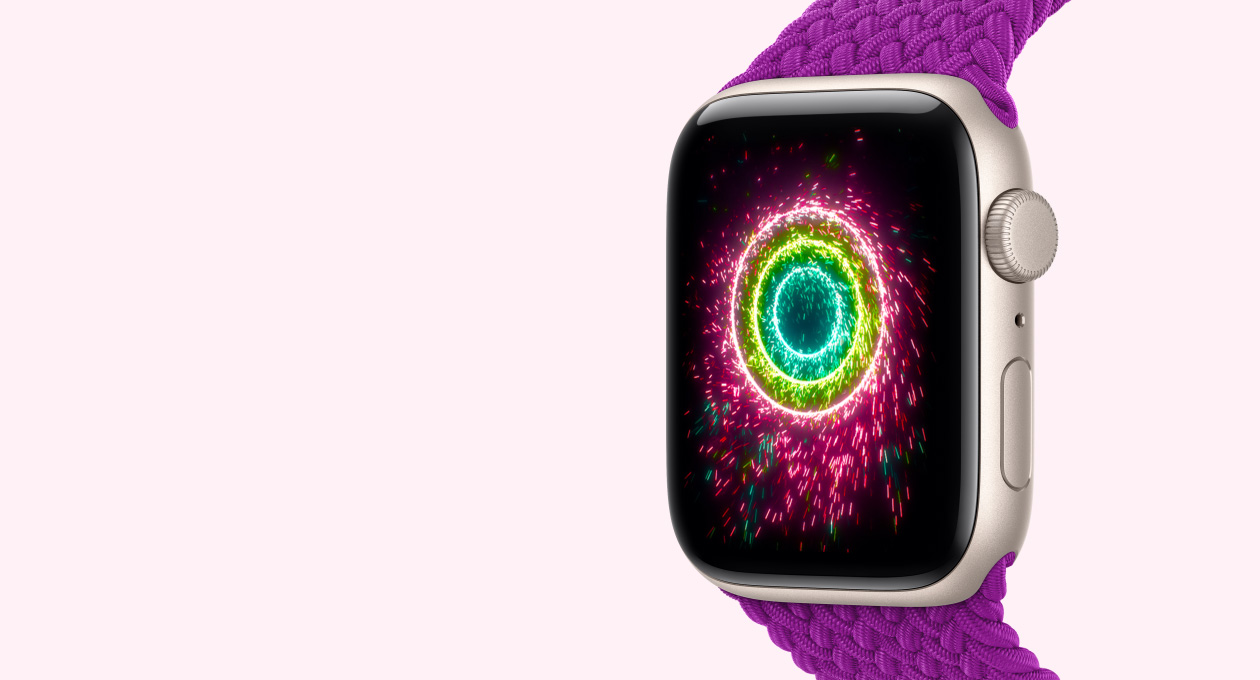 Apple Watch SE 3, hvězdně bílé hliníkové pouzdro s magentovým pleteným navlékacím řemínkem, na displeji je animace kroužků aktivity jako růžových, limetkově zelených a světle modrých jisker spojených do soustředných kruhů