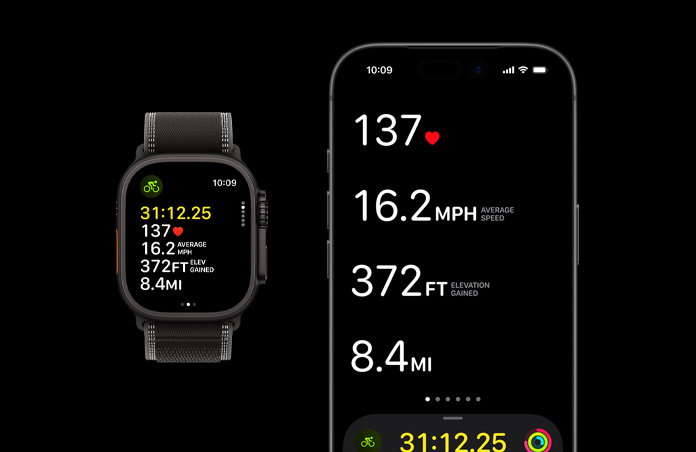 Apple Watch Ultra 3 med urkasse i sort titanium og Trail Loop-rem i sort/koksgrå og en iPhone, aktive træningsmålinger er åbne på begge enheder