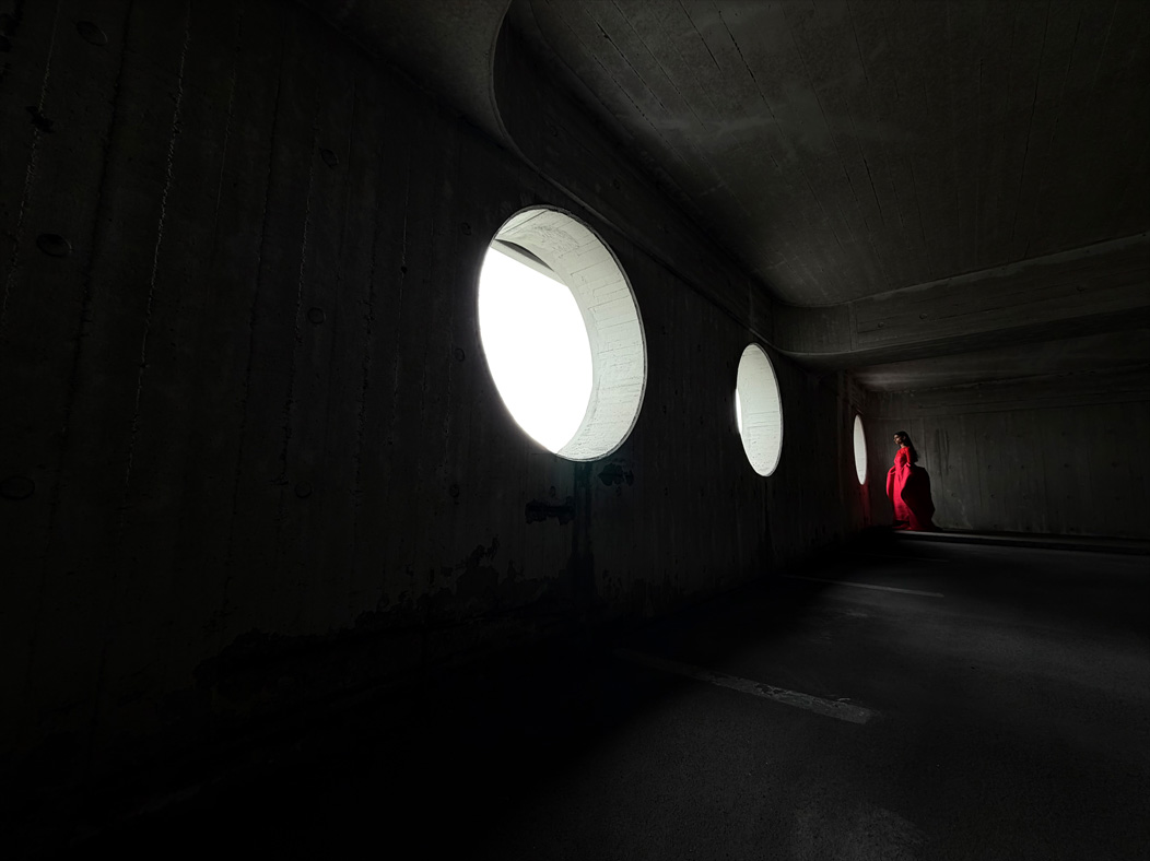 Uma mulher de vestido vermelho longo está sendo fotografada em um ambiente vazio. O app Fotos alterna entre as distâncias focais para demonstrar os recursos do sistema de câmera Pro, mostrando: 13 mm
