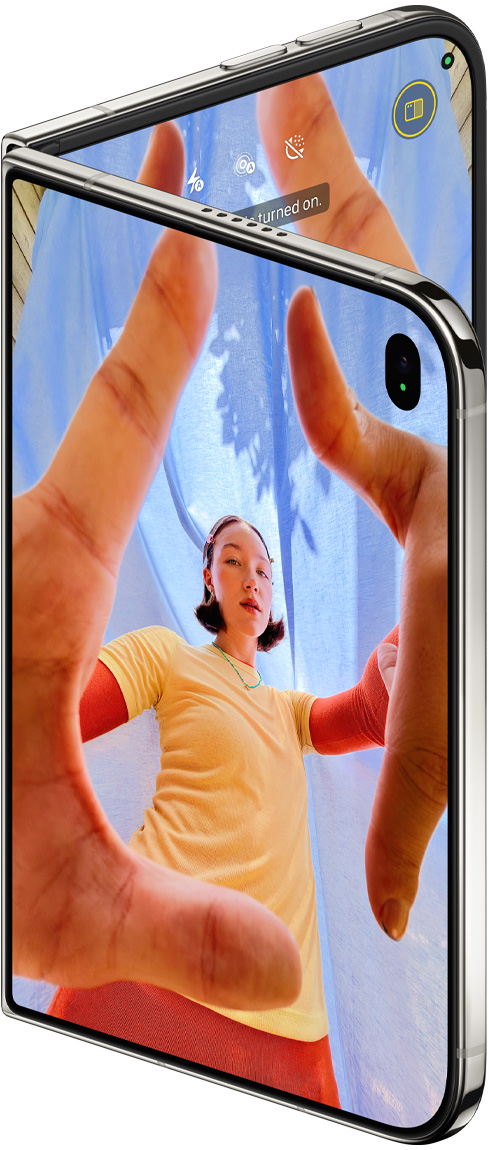 iPhone Duo, Star White colour, slightly open, Camera app on outer display with Center Stage front camera, inner display shows Photos app library