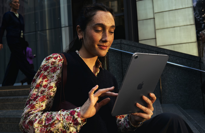 Person sitting on steps outside a large building using an iPad Air 11 in Space Grey, maintaining seamless Wi-Fi connection across network transfers
