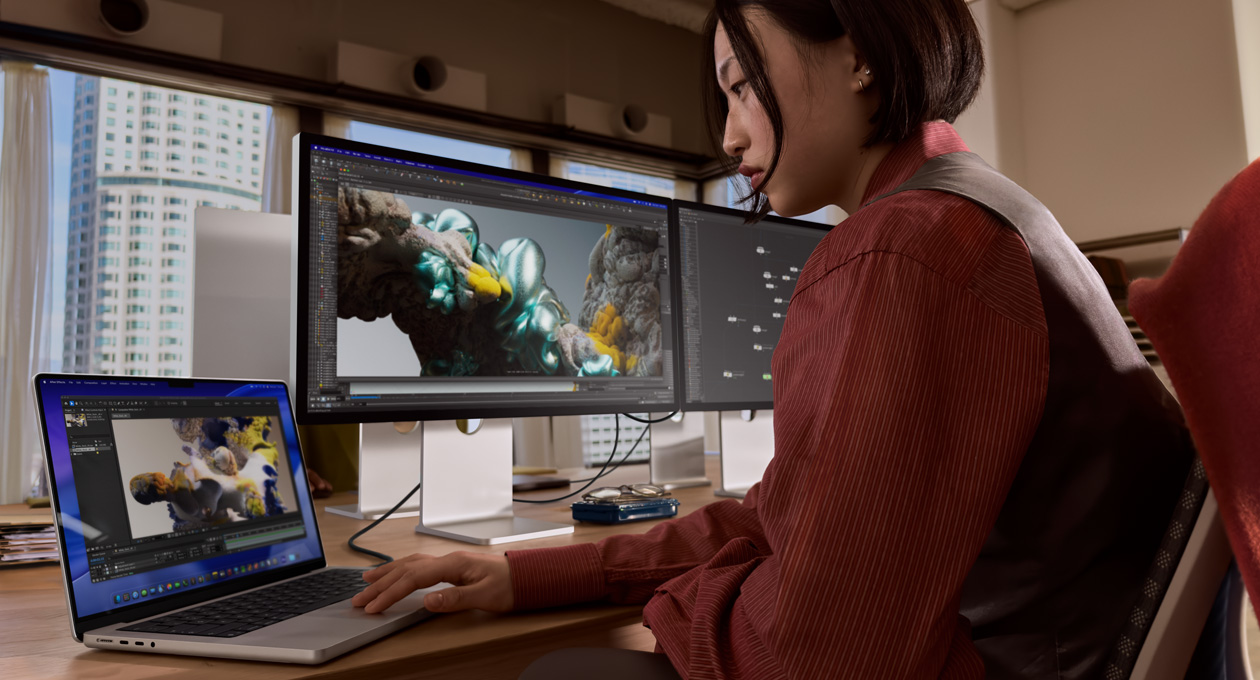 한 사람이 사무실에서 Thunderbolt 5 포트로 Studio Display XDR에 연결된 MacBook 노트북으로 작업 중인 모습